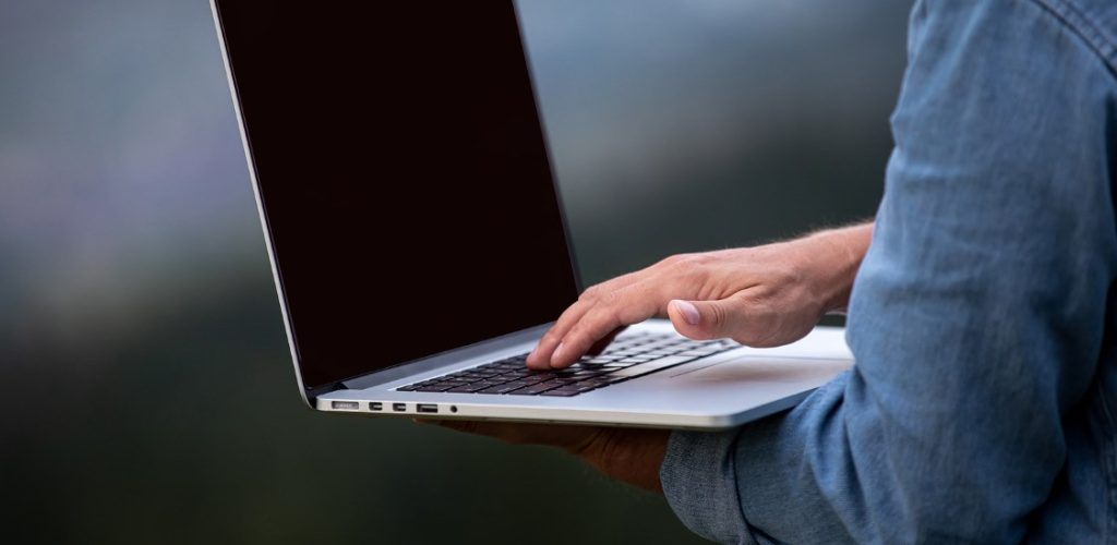 Man Working Outdoors With Laptop In Mountains. Concept Of Remote